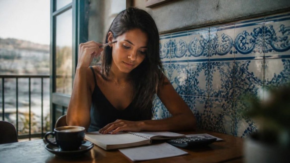 Brasileira planejando o orçamento com o salário mínimo 2027 em Portugal num café com azulejos